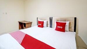 Een hotelkamer met een bed, een houten nachtkastje en een hoofdeinde met twee rode kussens.