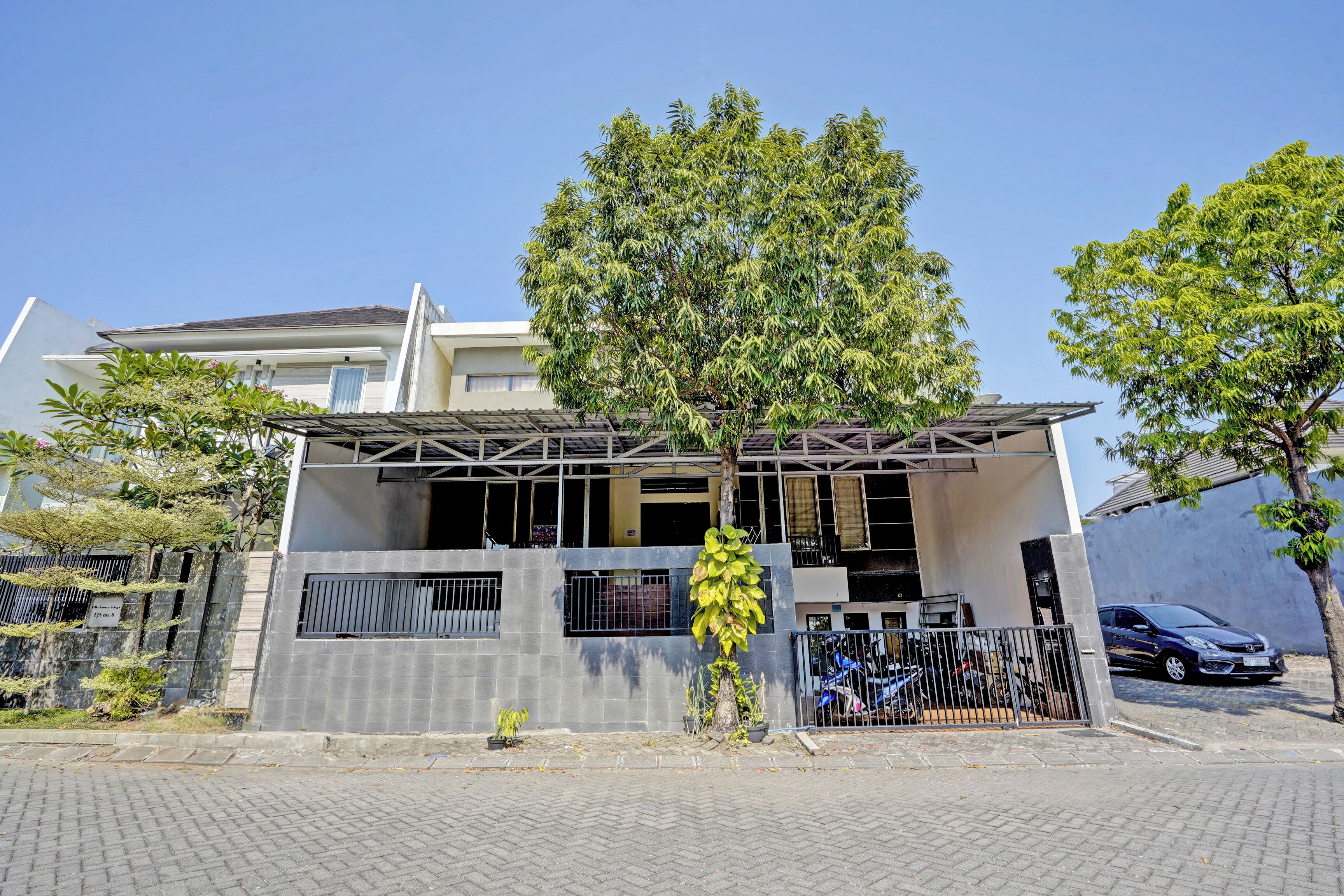Une maison moderne à deux étages, dotée d’un porche abrité, d’une allée fermée par un portail et d’un arbre en premier plan.