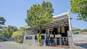 Een gebouw met twee verdiepingen, een overdekte parkeerplaats en een boom ervoor.