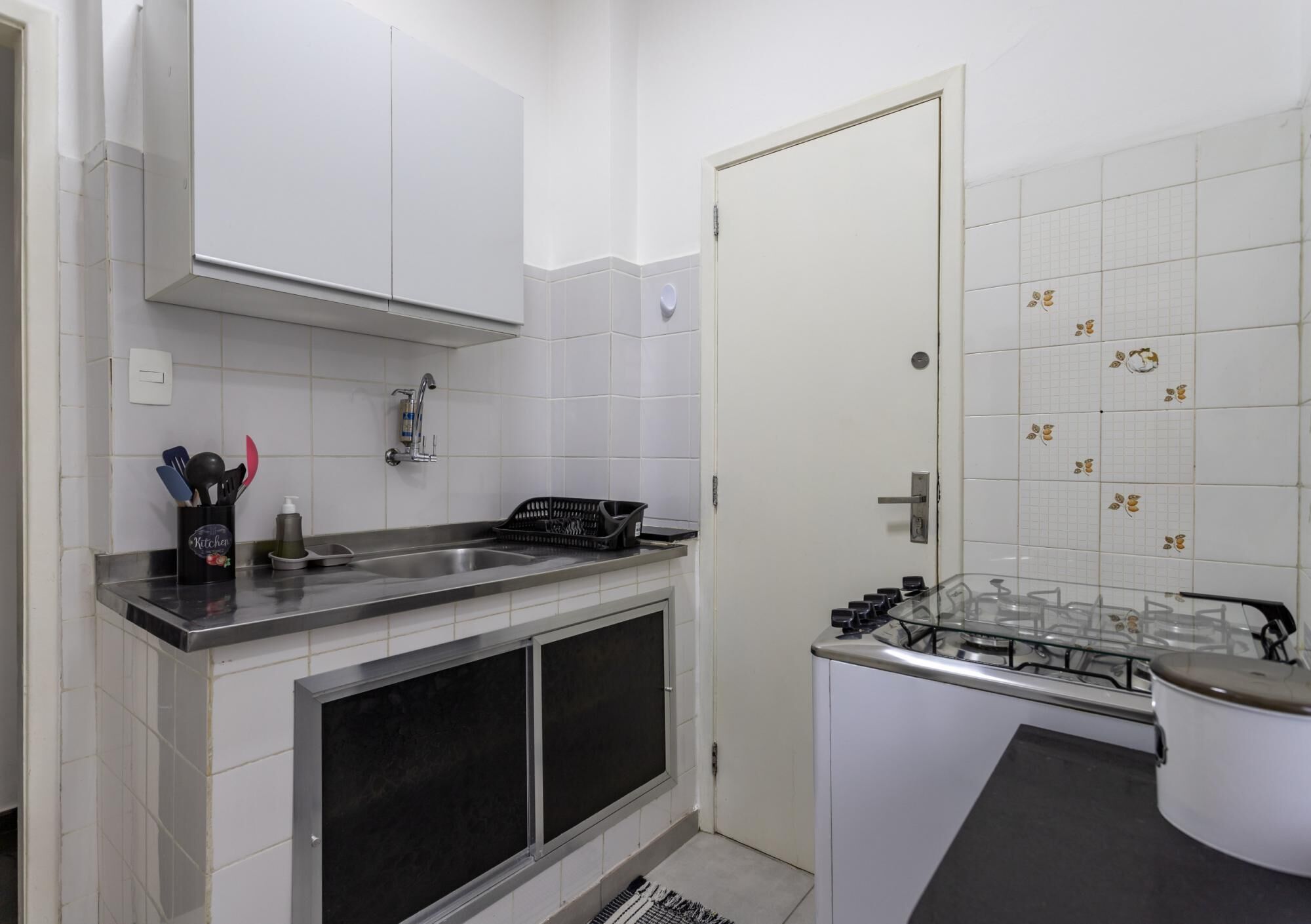 Una cocina compacta con gabinetes blancos, estufa a gas y un lavamanos.