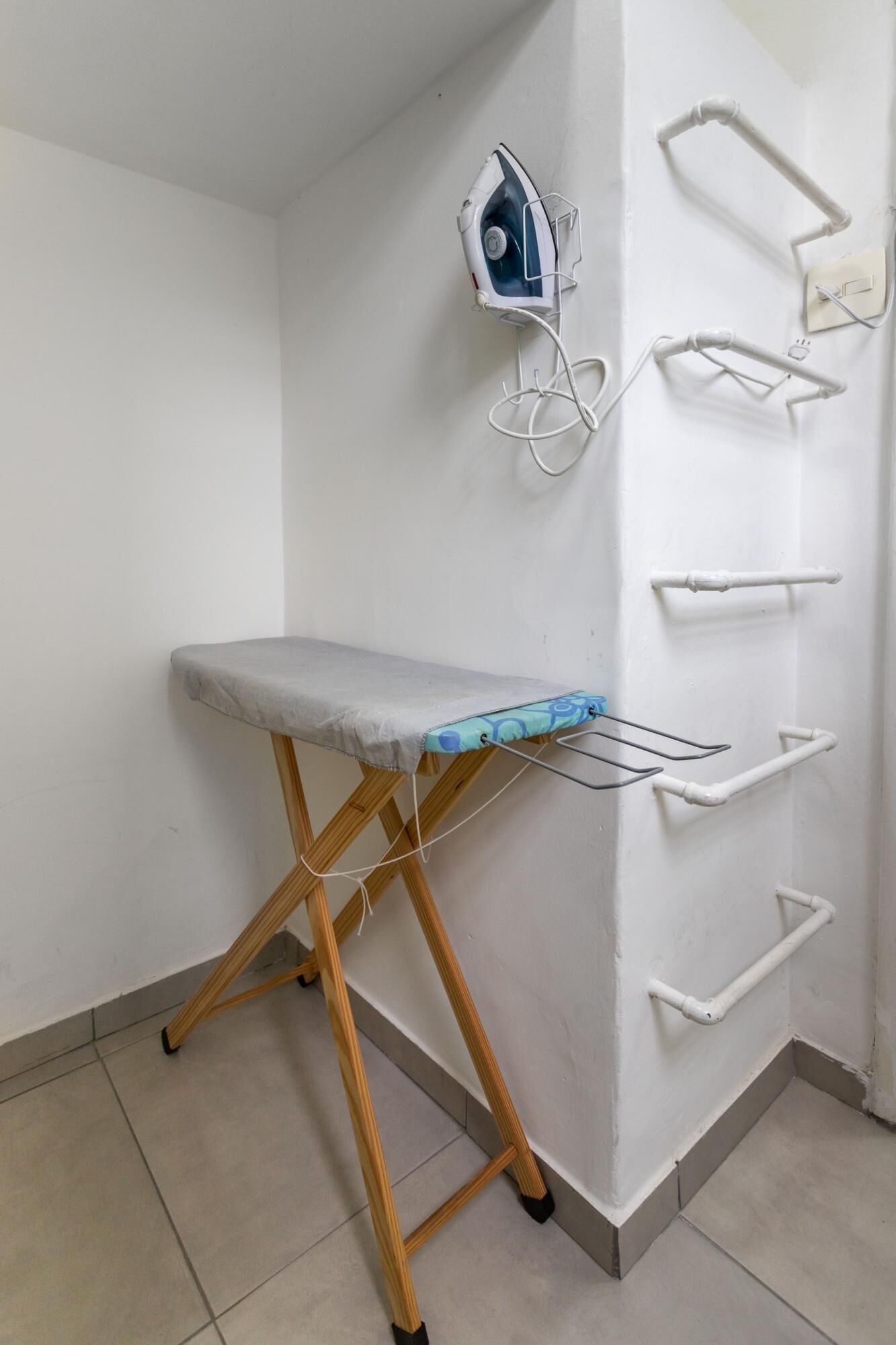 Una habitación compacta con una tabla de planchar de madera, una tabla de planchar fijada a la pared y un tendedero.