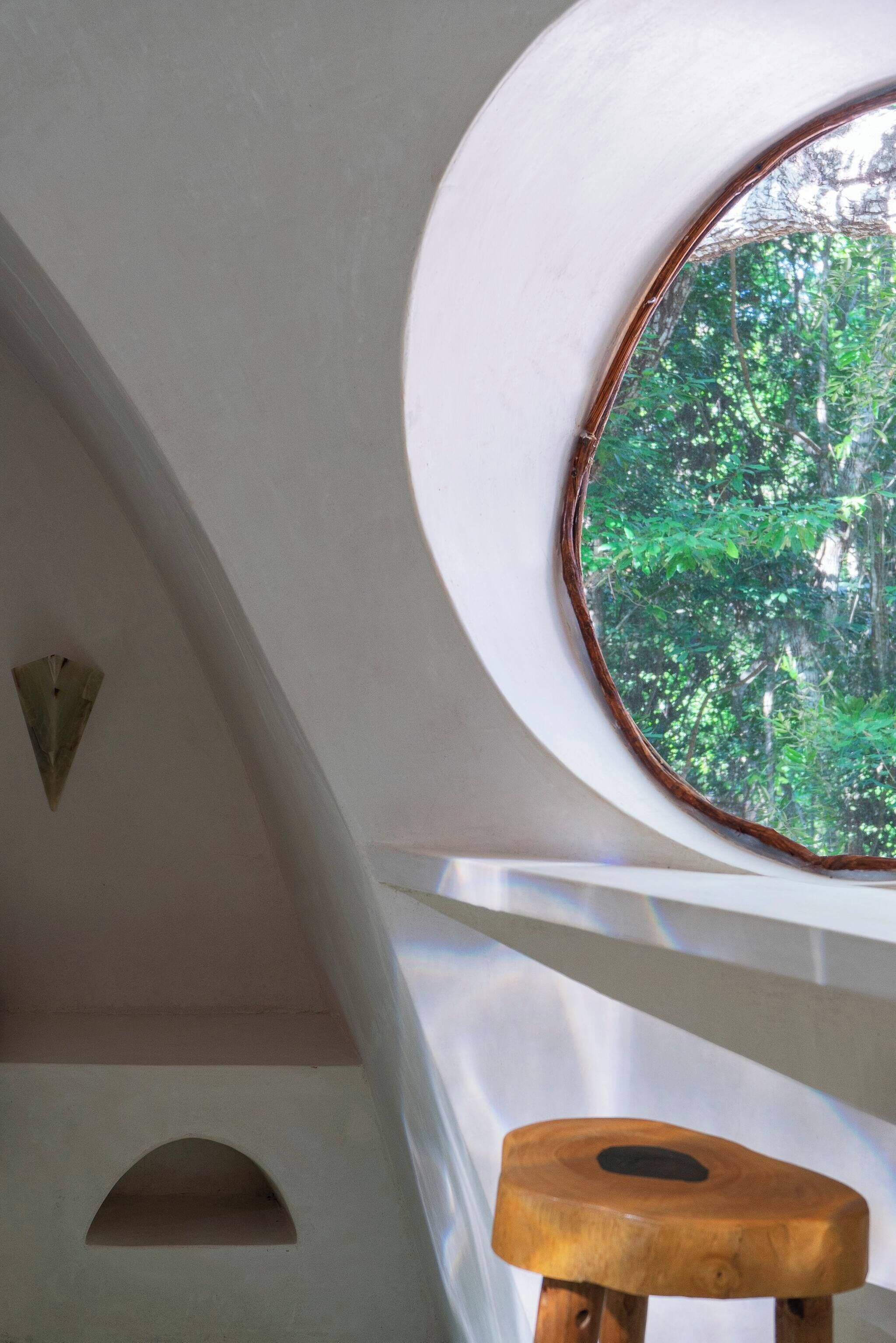 Una habitación con tragaluz, un taburete de madera y una pared blanca con un adorno triangular.