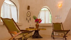 Ein Zimmer mit zwei Holzstühlen, einem kleinen Tisch mit Blumenvase und einem Fenster mit Vorhängen.