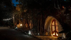 Ein naturbelassener, von Bäumen gesäumter Pfad führt zu einer gemütlichen, beleuchteten Hütte mit Bogenöffnung.