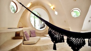Una habitación acogedora con una hamaca, ventanas circulares y un banco de piedra.