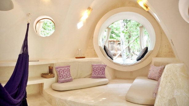 Una habitación acogedora y circular con un ventanal redondo, asientos mullidos y una hamaca colgante.