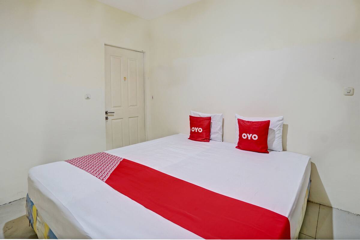 Une chambre d’hôtel avec un lit, des murs blancs, une porte et deux oreillers sur lesquels est inscrit le mot « OYO ».