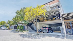 Un bâtiment moderne à deux étages, doté d’un espace de stationnement couvert, d’un escalier et d’un arbre aux fleurs jaunes.