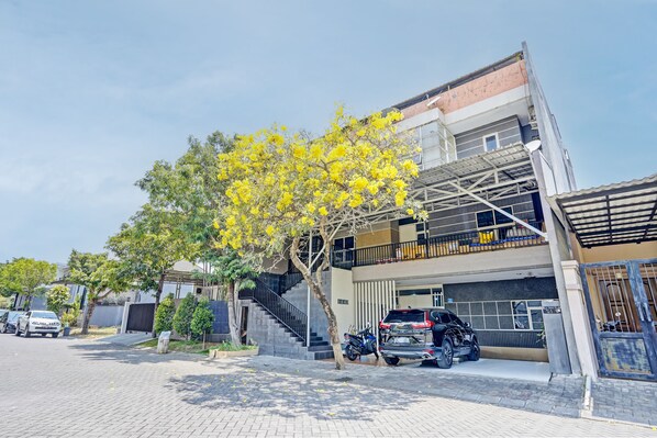Two-story building with a balcony and garage entrance, set amidst a tree with blooming flowers.