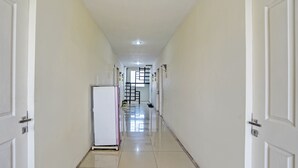 Un couloir aux murs blancs, doté d’un sol carrelé et d’un réfrigérateur placé sur le côté gauche.
