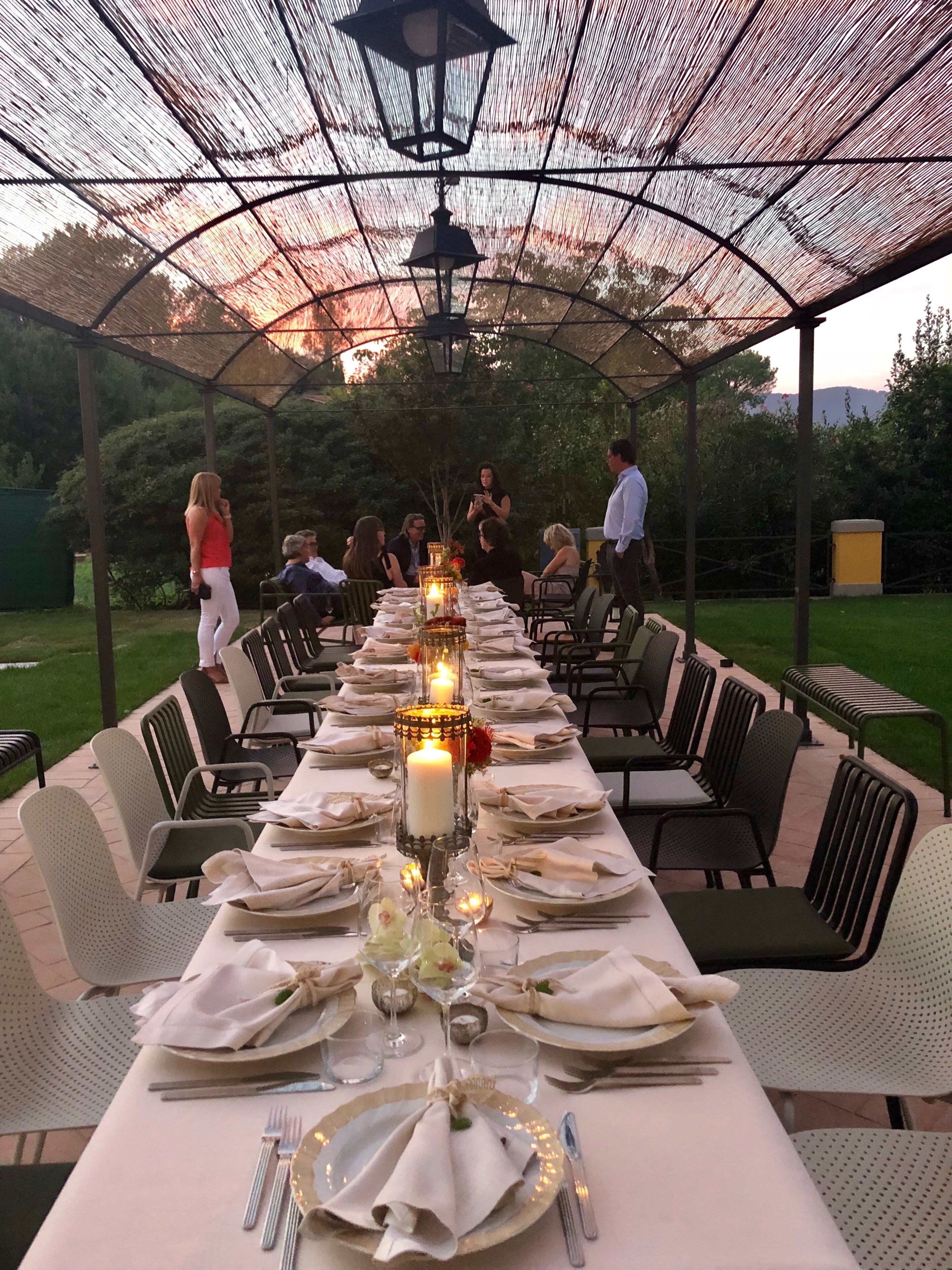 An outdoor dining area with a long table set for a meal, surrounded by chairs, and a canopy overhead.