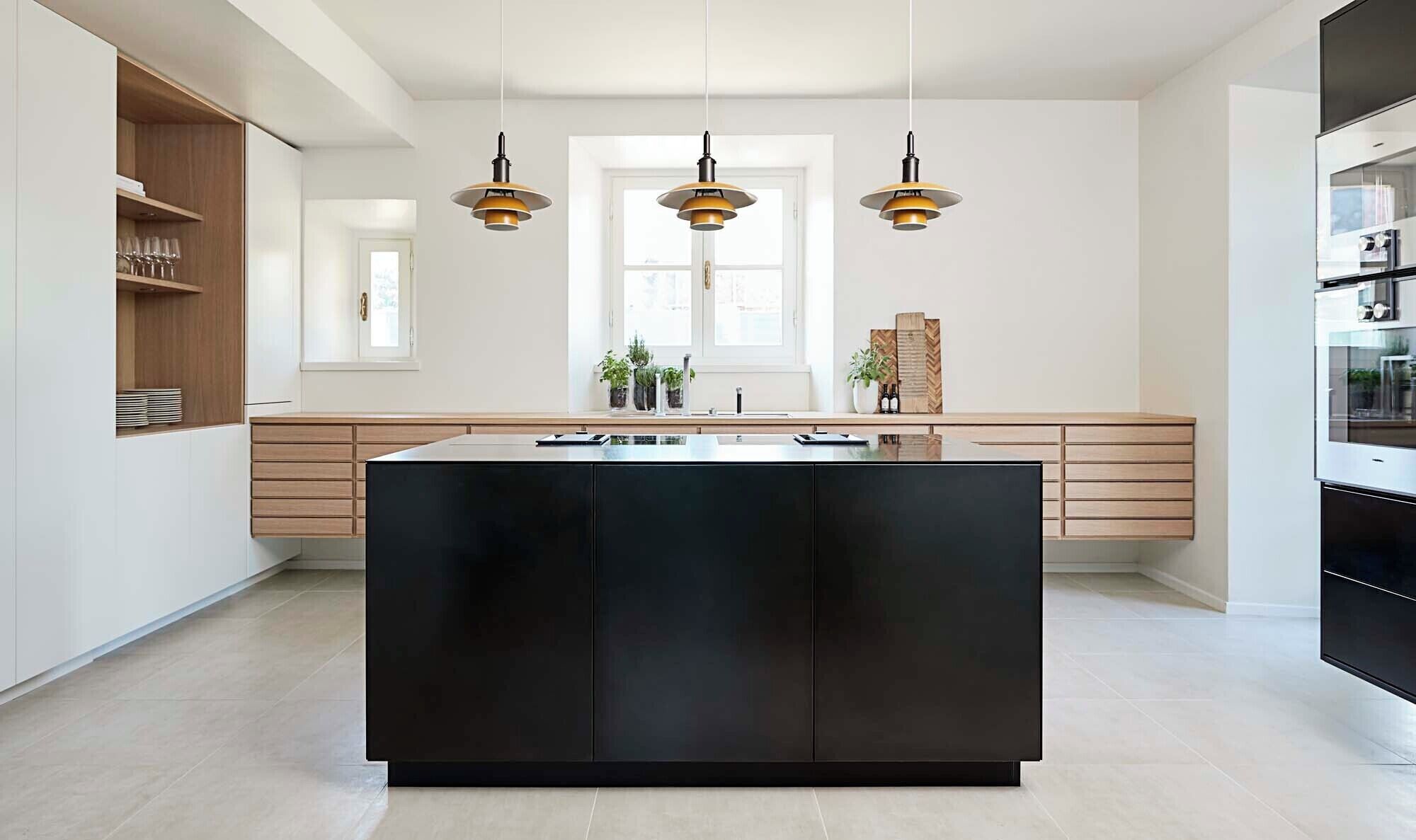 A modern kitchen with a central island, pendant lights, and a view to the outside.