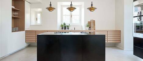 A modern kitchen with a central island, pendant lights, and a view to the outside.
