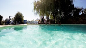 Une piscine à l’eau claire, entourée d’un mur de pierre et d’arbres.