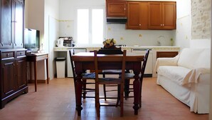 Une cuisine avec des meubles en bois, une table à manger avec des chaises, un canapé blanc et un téléviseur posé sur un meuble.