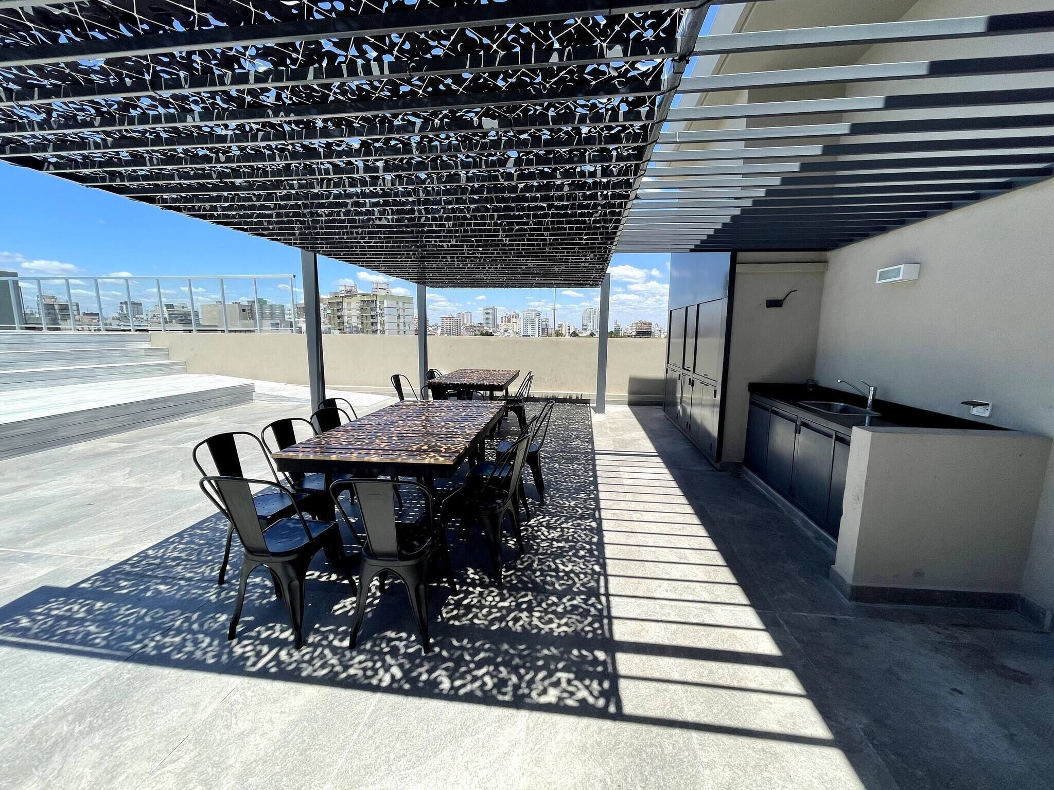 A rooftop patio with a table and chairs, a grill, and a view of the city skyline.