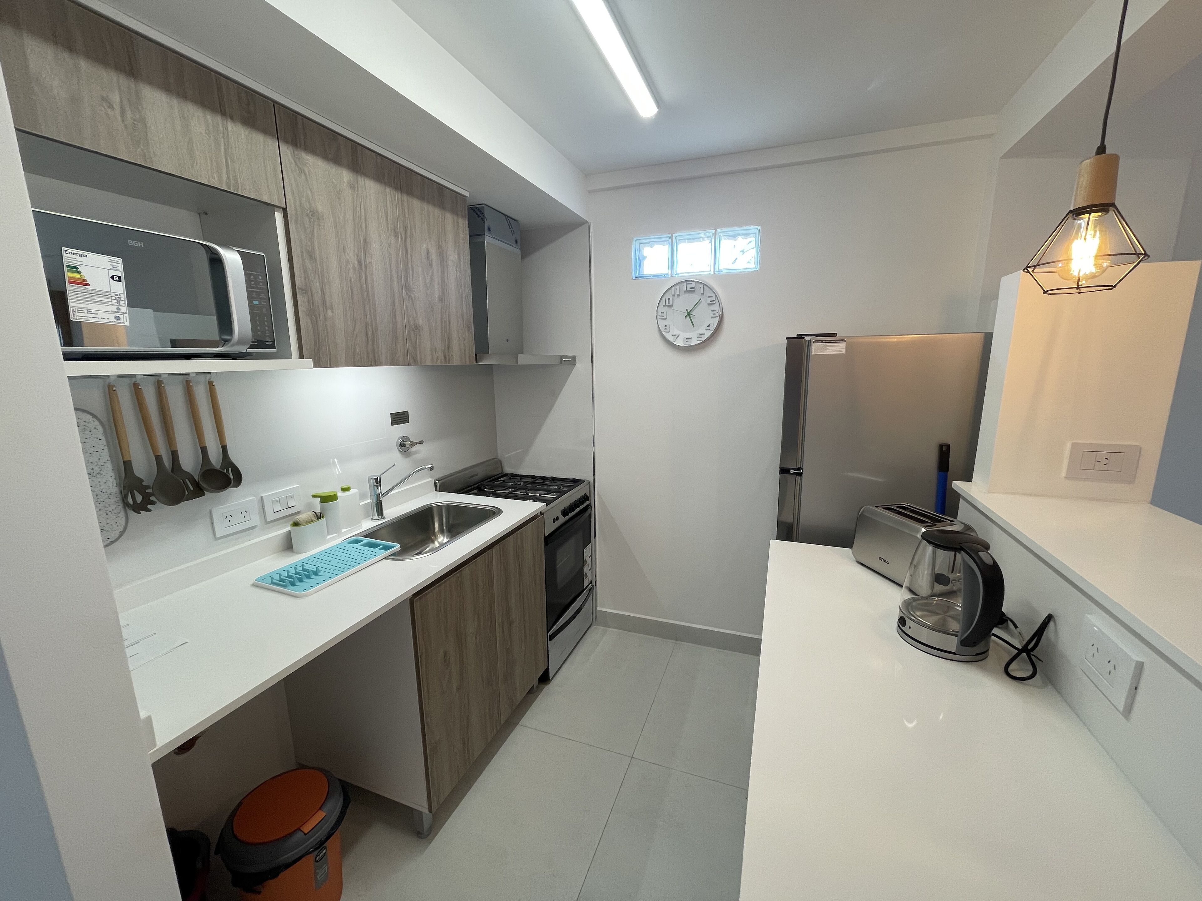 Una cocina compacta con microondas, estufa, pileta y un reloj en la pared.