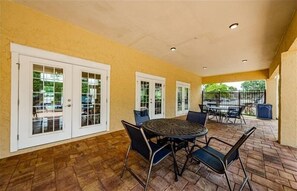 Relax in this inviting patio area with a round table and six chairs, surrounded by a wall and glass doors leading to the outside.