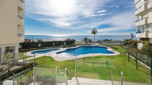 A swimming pool with a curved design, surrounded by a well-maintained lawn and a clear view of the ocean.