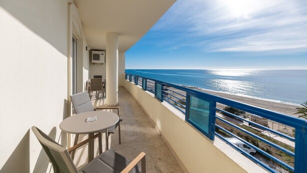 A balcony with a table and chairs, overlooking a beach and the ocean.