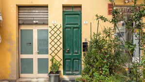 A yellow building with a green door, a window with frosted glass, and a door number sign.