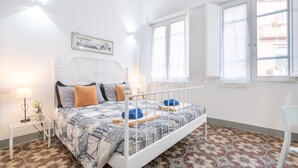 A bedroom with a bed, a bedside table, a lamp, a window, and a patterned floor.