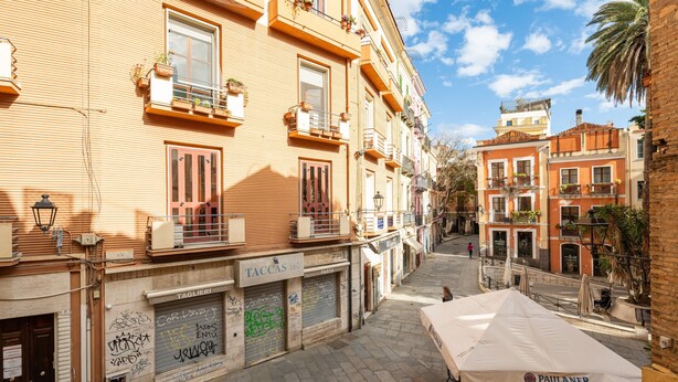 A narrow street with buildings, outdoor seating, and a clear sky.
