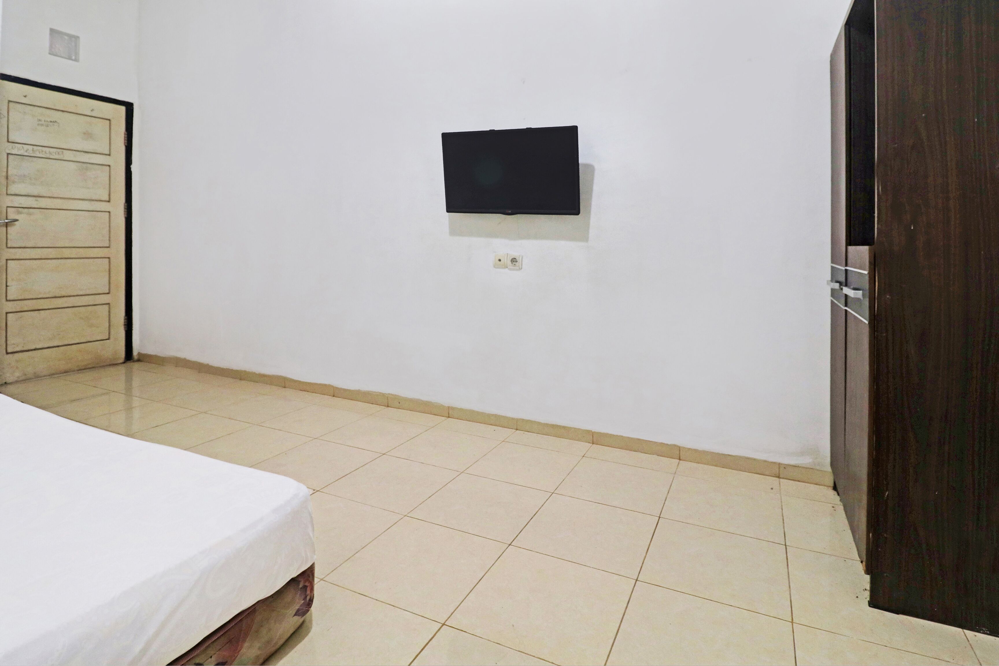 Une pièce avec un lit, un téléviseur fixé au mur et une porte.