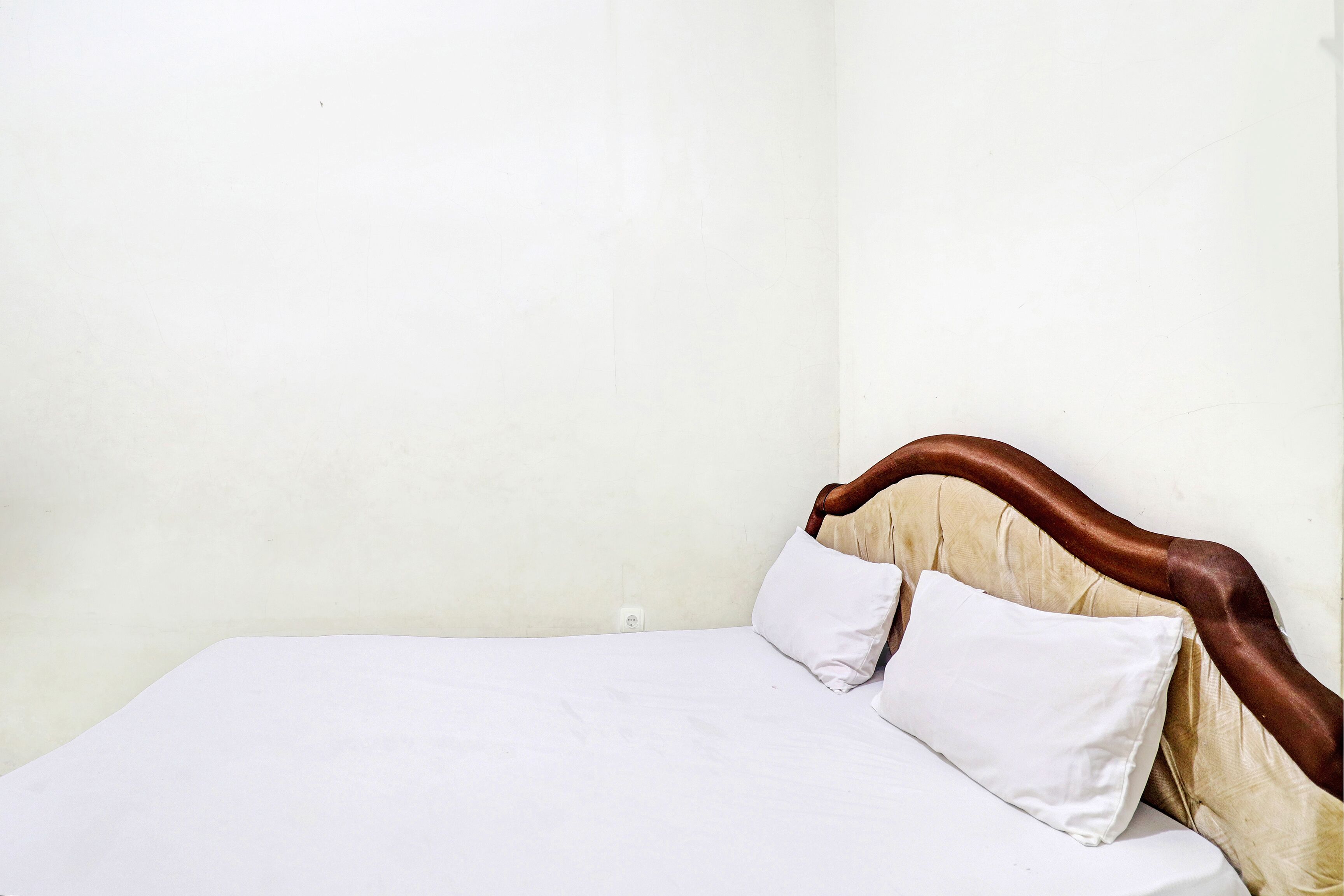 Una cama individual con cabecera de madera y dos almohadas blancas en una habitación con paredes lisas.