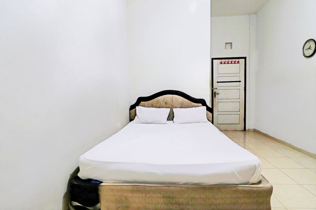 A single bed with white bedding in a small, narrow room with white walls and a tiled floor.
