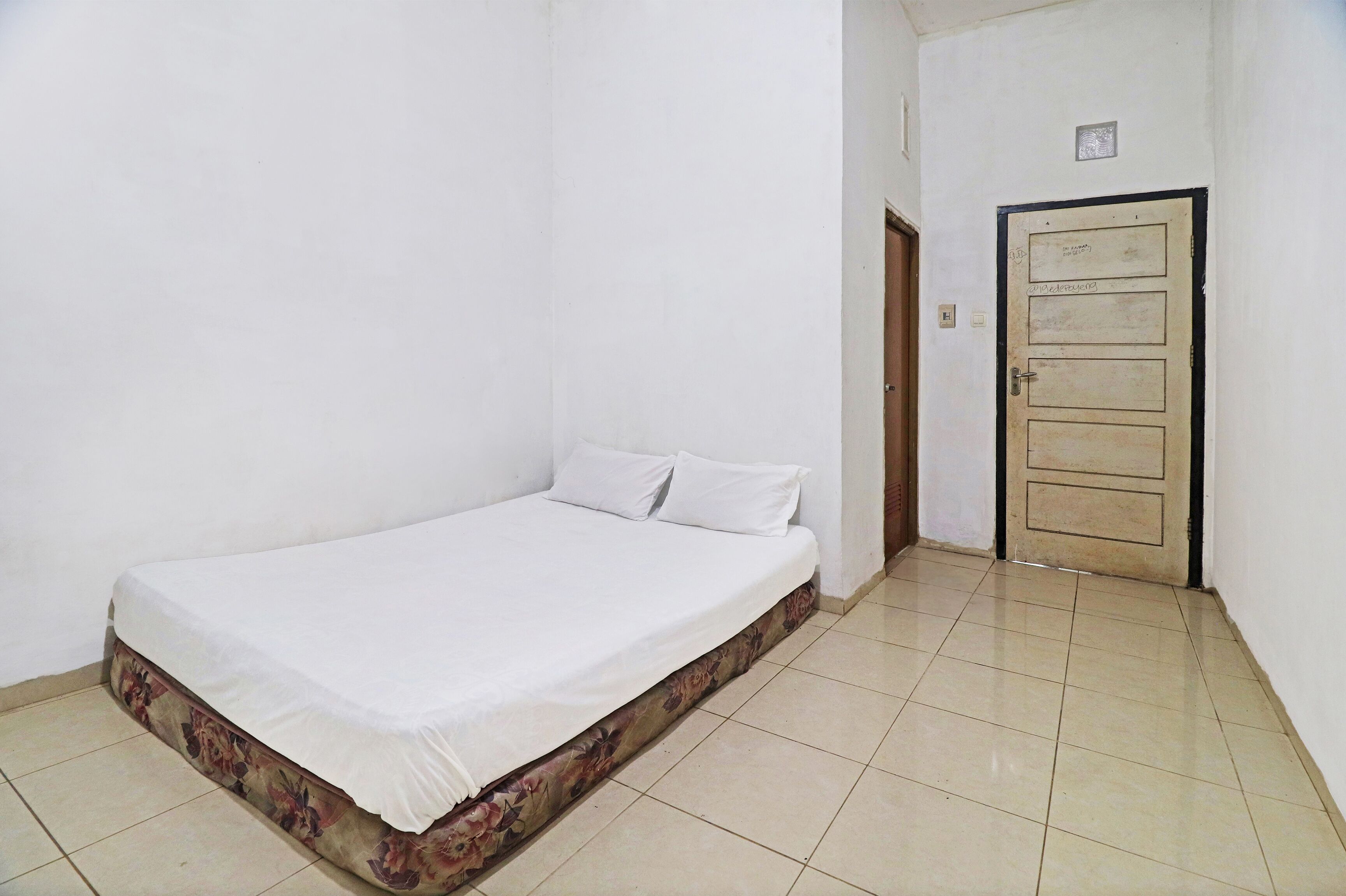 A small, clean room with a single bed, a door, and tiled flooring.