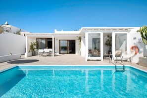 A modern poolside area with a clear blue pool, white walls, and a covered seating area with chairs. - Villa "El Ancla" with Sea View, Private Pool and Wi-Fi (Playa Blanca)