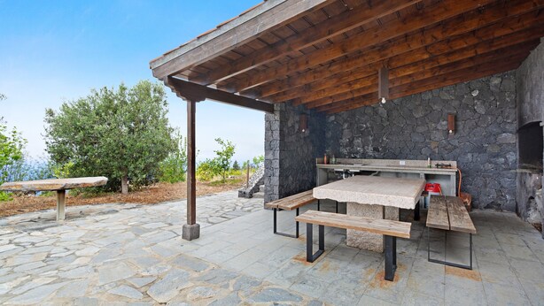 Eine Terrasse im Freien mit Steinböden, Holzbanken, einer Steinwand und Grillplatz.