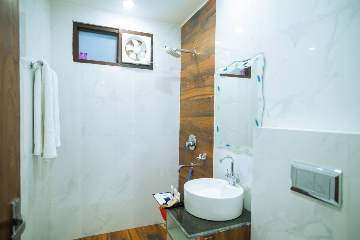 A modern bathroom with a marble wall, a wooden panel, a white sink, and a handheld showerhead.