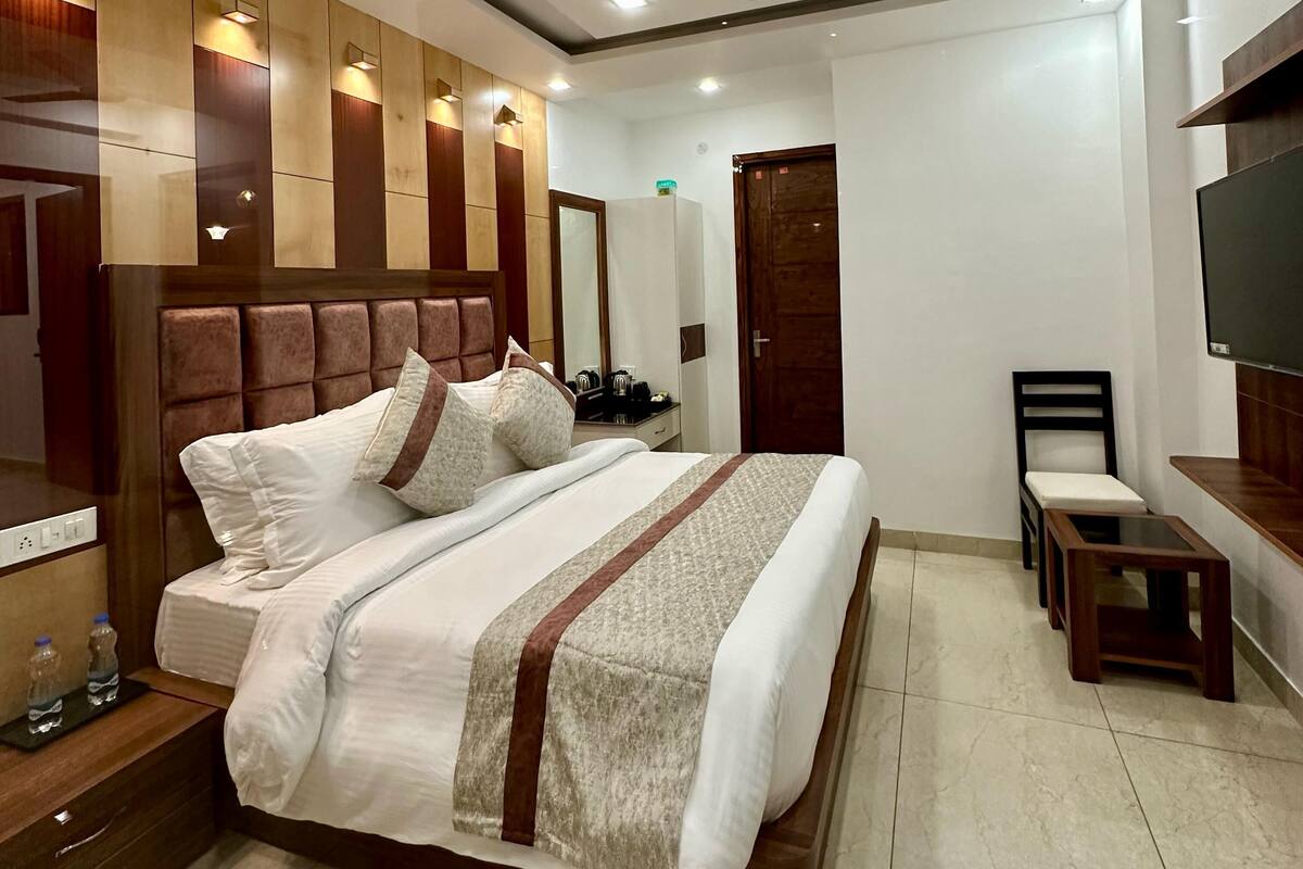 A hotel room with a large bed, a wooden headboard, a TV mounted on the wall, a small table, and a chair.