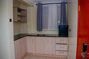 Una cocina compacta con armarios de madera clara, encimera negra, un fregadero y un refrigerador.