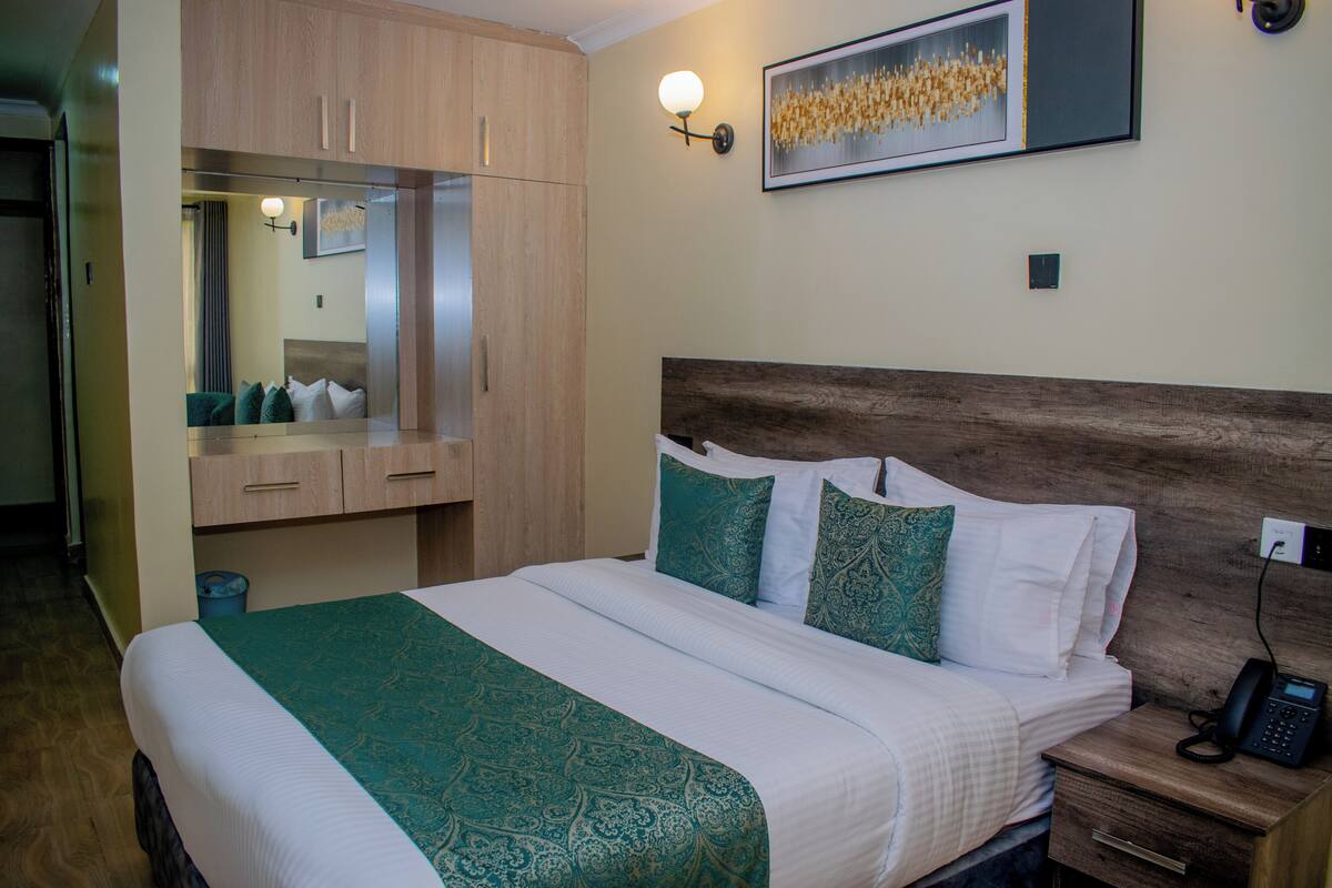 A hotel room with a large bed, a wooden headboard, a bedside table with a phone, and a mirror above the bed.