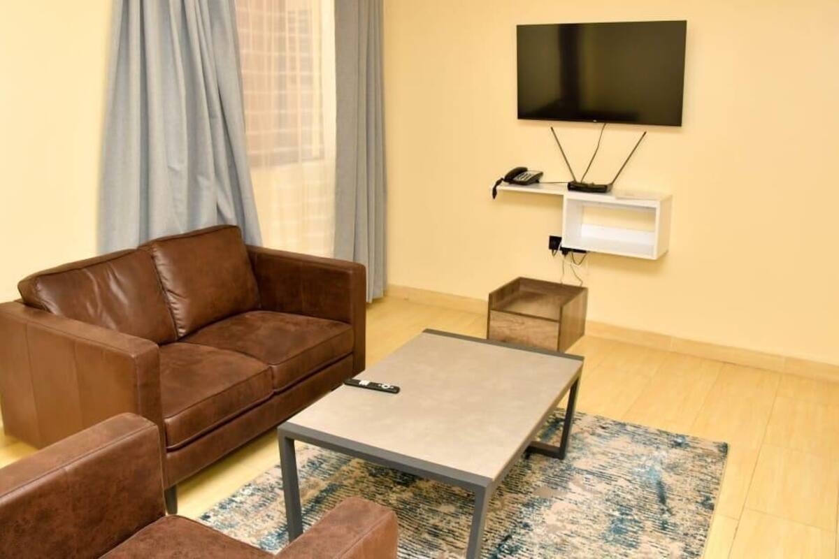 A modern living room with a brown leather sofa, a small coffee table, and a TV mounted on the wall.