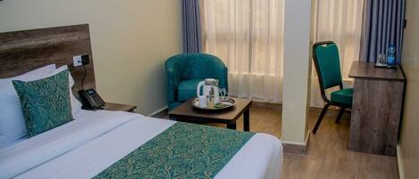 A hotel room with a large bed, a desk, a chair, and a coffee table.