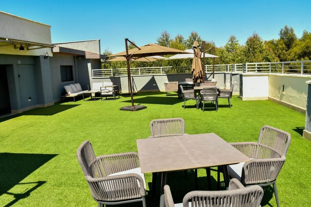 Une terrasse extérieure avec une table et des chaises, entourée d’une balustrade blanche et de verdure.
