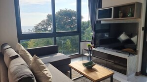 Ein modernes Wohnzimmer mit großem Fenster, einer Couch, einem Couchtisch und einem Fernseher.