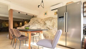 A modern kitchen with a stainless steel refrigerator, a dining table with chairs, and a large rock wall. - The Rock Star's Villa With Private Pool And Beach (Novo Selo)