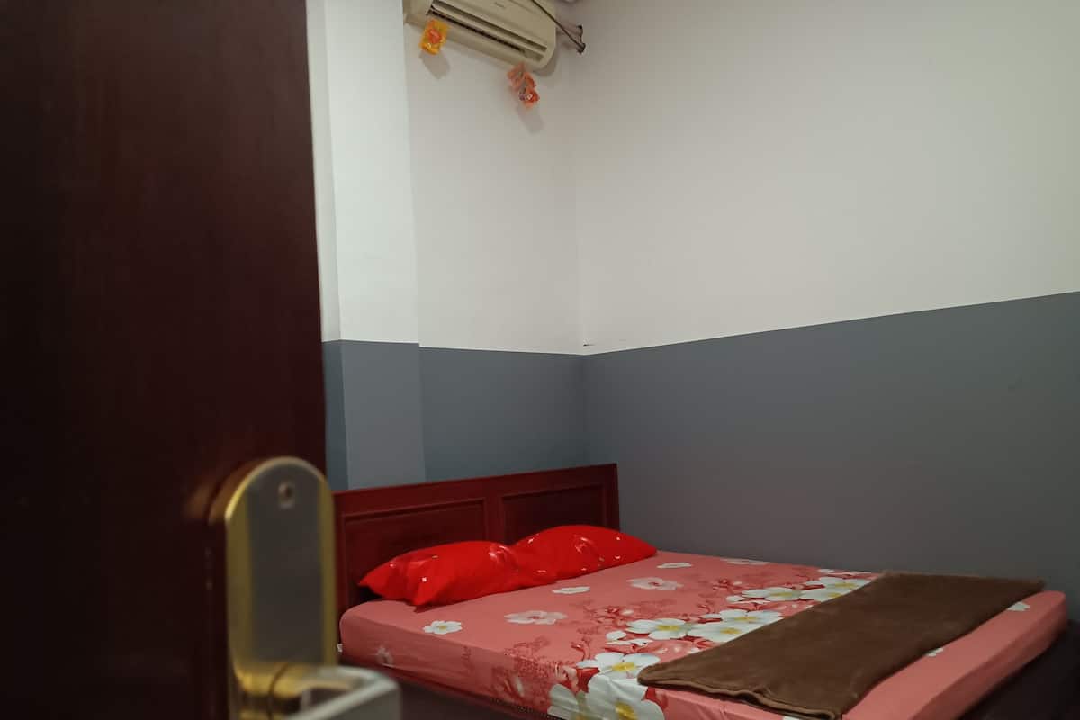 A bedroom with a bed, a wooden headboard, a red pillow, a floral bedspread, and a brown blanket.
