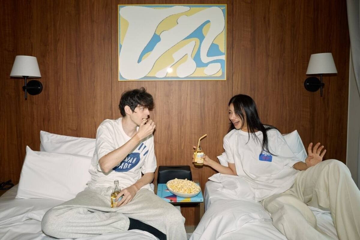 Habitación de hotel con paredes de madera, dos lámparas de noche, un cuadro abstracto de gran tamaño y una bandeja con palomitas y bebidas sobre la cama.