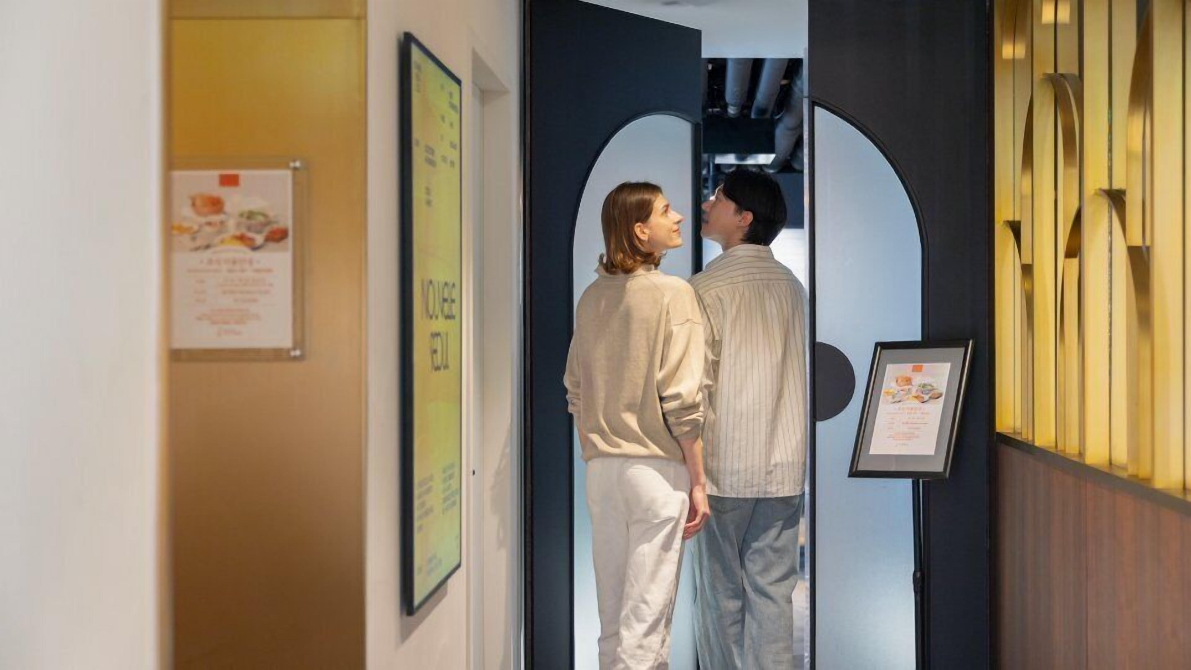 A hallway with framed menus on the walls, a door with a circular cutout, and a wooden panel with vertical slats.