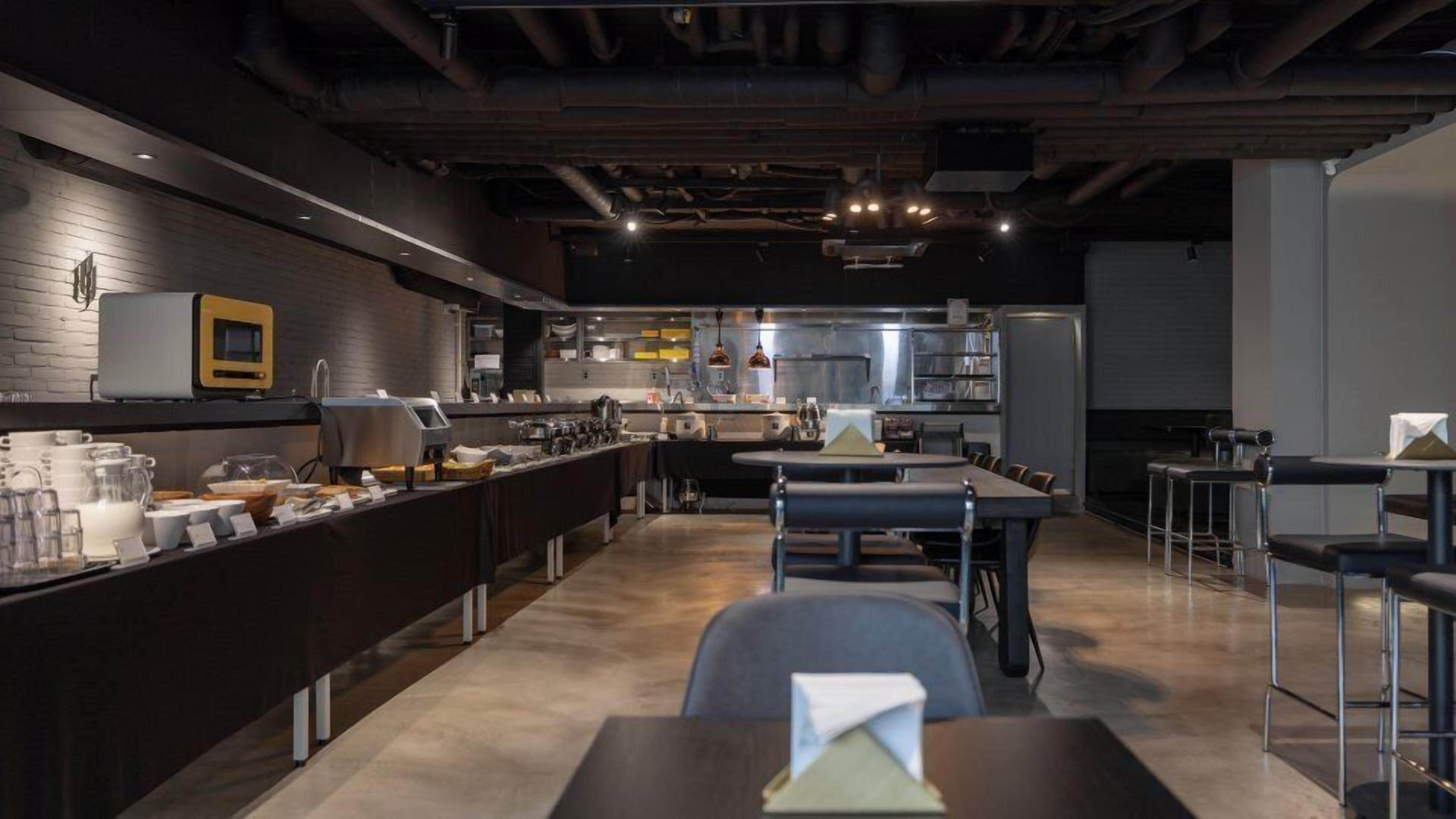 Un restaurante moderno con una barra larga, varias mesas y una zona de cocina al fondo.