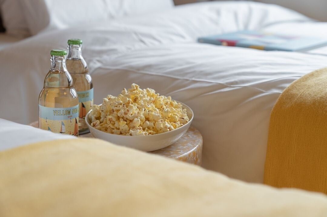 Ein Bett mit weißen Laken, eine Popcornschale und zwei Flaschen gelben Limonaden.