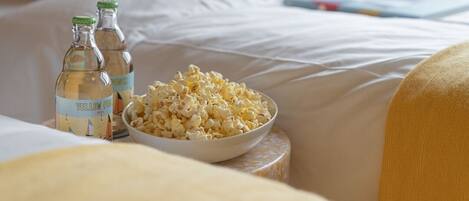 Ein Bett mit weißen Laken, eine Popcornschale und zwei Flaschen gelben Limonaden.