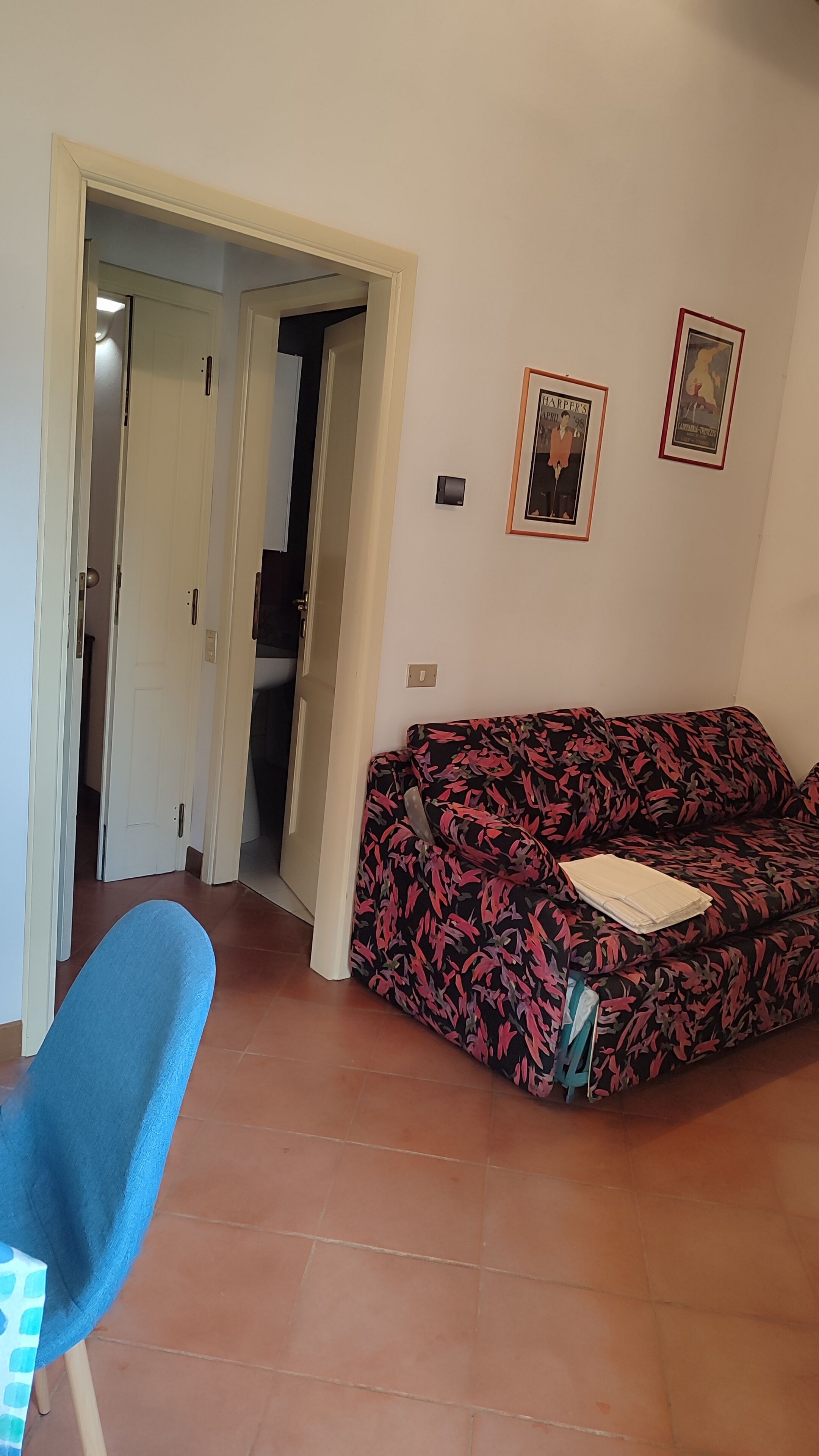 Een woonkamer met een bank, een deur naar een andere kamer, en twee ingelijste foto's aan de muur.
