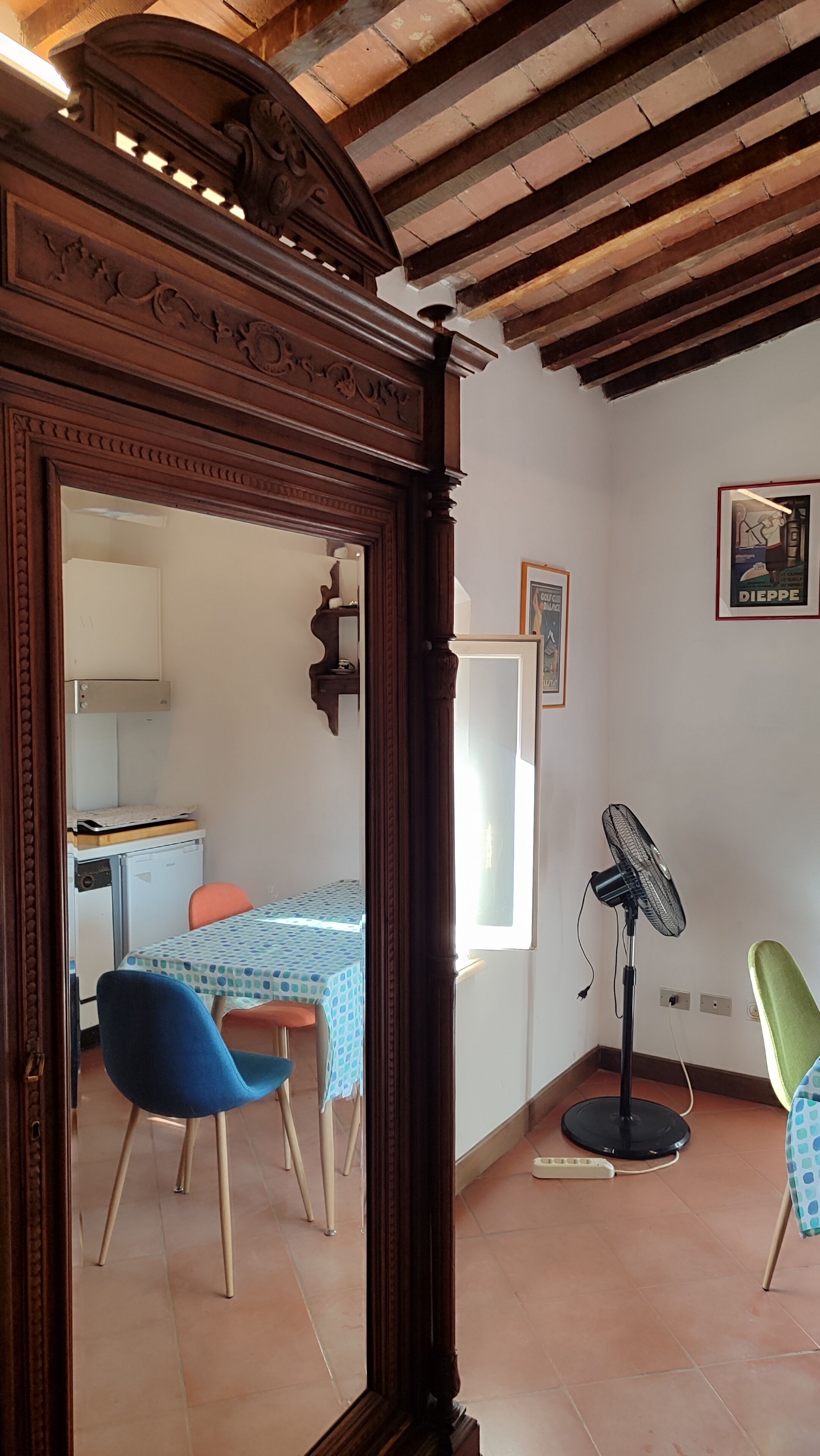 Una habitación con techo de madera, una mesa de comedor con sillas, un ventilador de pie y un cuadro en la pared.